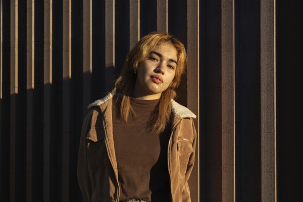 A Mixed-race woman leans against a textured wall, bathed in warm sunlight Her casual outfit and
