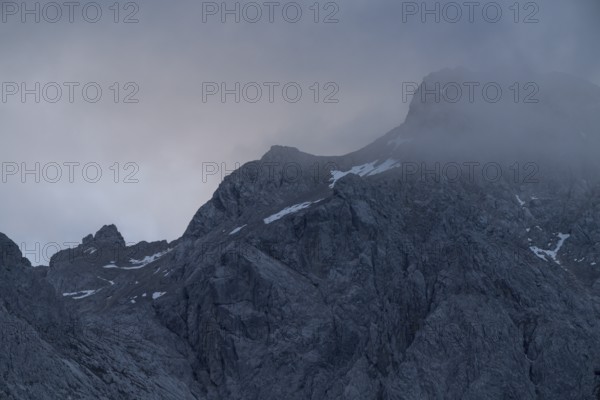 A dramatic view of towering peaks in the Bavarian Alps, partially covered by swirling mist The