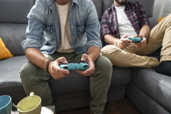 A gay couple sits on a couch, immersed in a video game. They both hold controllers, wearing casual