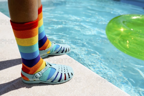 A vibrant scene featuring rainbow-striped socks paired with blue sandals by a bright swimming pool.