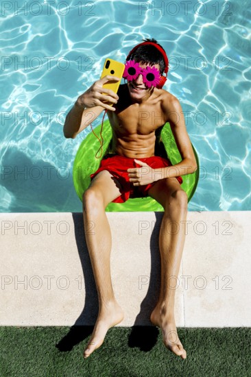 A young teenage boy relaxes on a float in a bright blue pool, wearing colorful flower-shaped