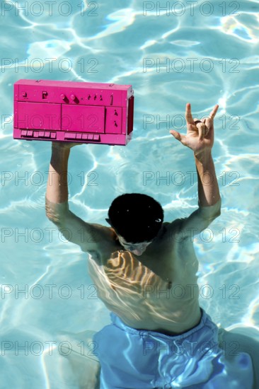 A person in blue shorts enjoys a sunny day in a pool, holding a vibrant pink boombox above the
