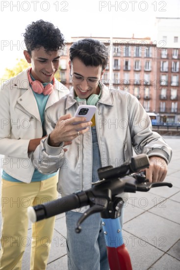 A happy gay couple, each wearing headphones, enjoys a light-hearted moment outdoors while looking