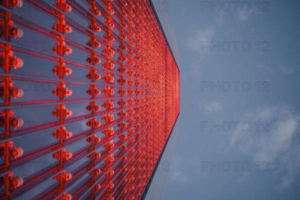 Dramatic upward view of a skyscraper with a red glass facade against a blue sky. The modern