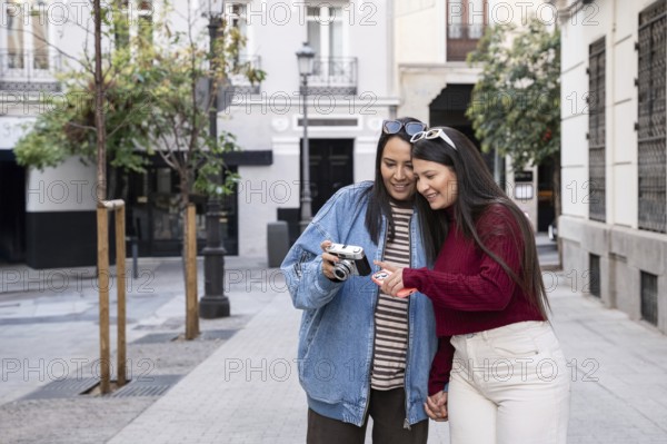 A happy latin lesbian couple enjoys a day out, capturing memories with a camera. They share a