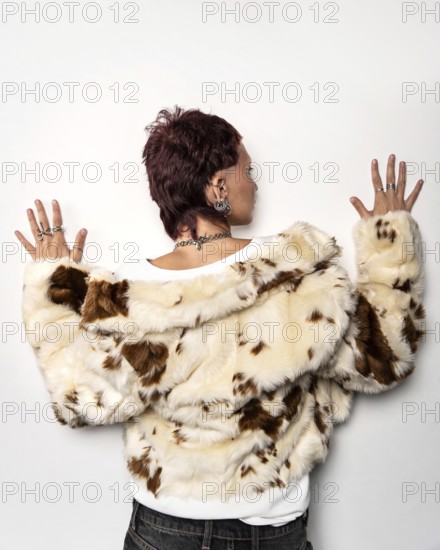 A woman with a trendy mullet hairstyle, adorned with earrings and rings, wearing a stylish cream