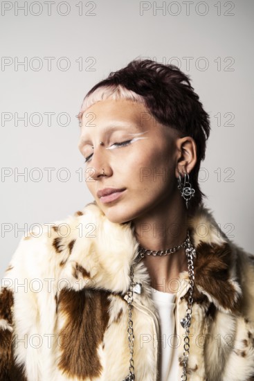 Close-up of a woman with a bold hairstyle, glamorous nose and ear piercings, striking white