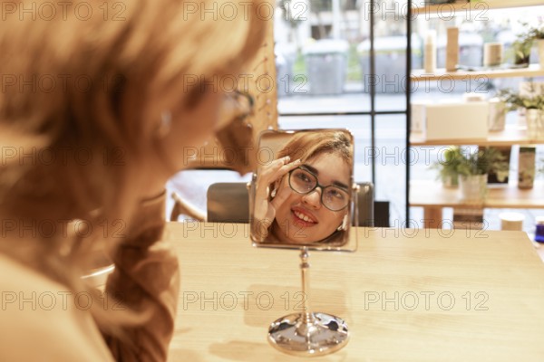 A smiling woman tries on a new pair of eyeglasses while looking at her reflection in a tabletop