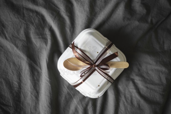 Top view of an elegantly wrapped bento birthday cake, set in a white takeout box with a brown