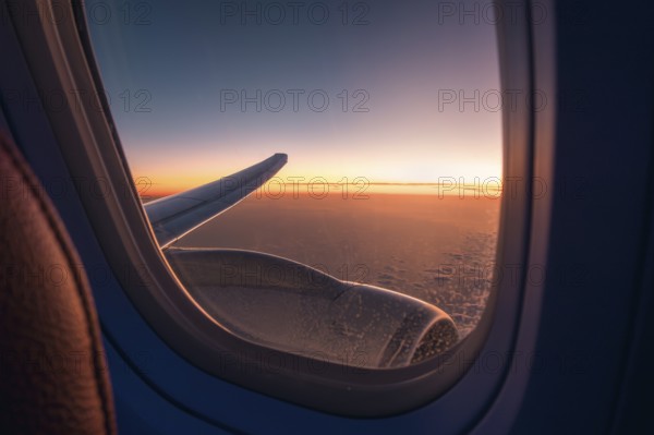 View through an airplane window catching the glowing sunset skyline above the clouds, with the
