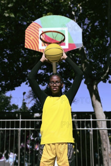 A black basketball player stands ready to shoot, holding a yellow basketball toward a vibrant,