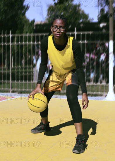 A focused woman basketball player dribbles a ball on a vibrant outdoor court. Dressed in a yellow