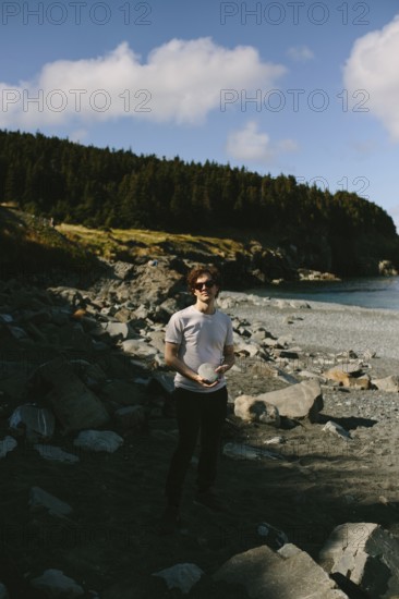 A young man stands on the rocky shores of Middle Cove in Newfoundland & Labrador, Canada. He is