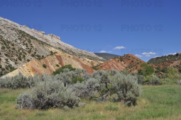 Rocks with colorful soil, vegetation and blue sky in hilly landscape, Dinosaur National Monument,
