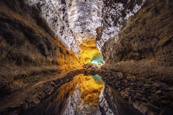 Lava tunnel, illuminated lava cave with perfect reflection in an underground lake, Cueva de los