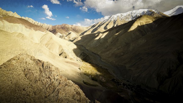 Dramatic mountain landscape with strong light and shadow in the valley, snow-capped mountains in