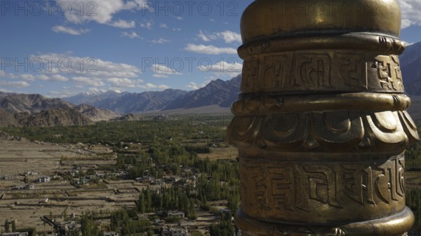 View from a monastery across the valley a golden prayer wheel in the foreground with a vast