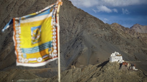 View of Namgyal Tsemo Buddhist mountain temple, with colorful prayer flags against a blue sky,