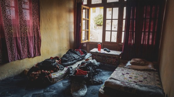 A simple room in a mountain village in the Indian Himalayas with two beds, backpack and cinder and