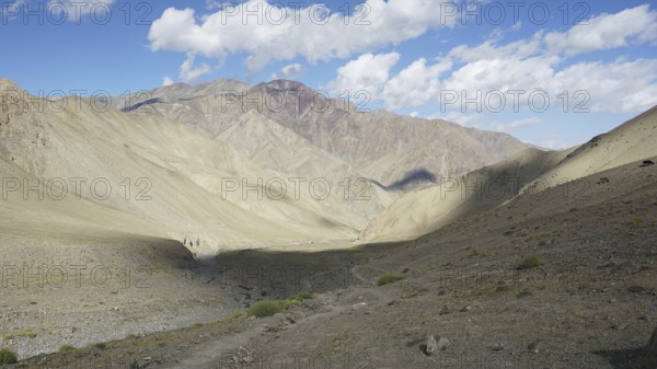 Wide mountain valley under a partly cloudy sky with a small path, trekking in Ladakh, Stok la,