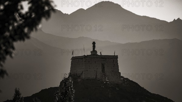 A monastery is majestically perched on a hill with mountains in the background at dusk, Leh,