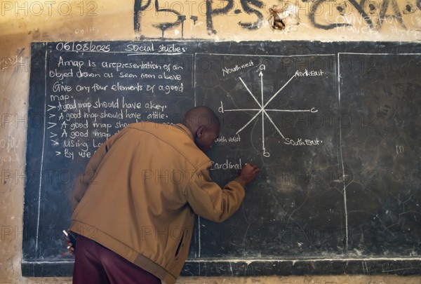 Teacher writes on a blackboard in a classroom during a lesson, school, Rushaga, Western Region,
