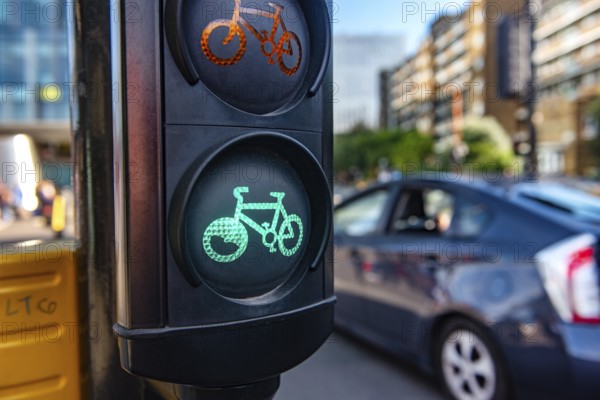 A green cycle lane traffic signal at a junction in a busy London city street with a car passing in