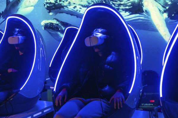 Young woman experiencing a virtual reality underwater whale and shark simulation, sitting in a