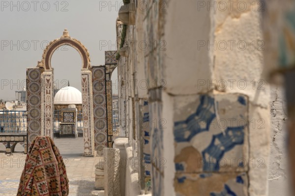 A rooftop view of a domed building through an archway decorated with traditional mosaic designs,
