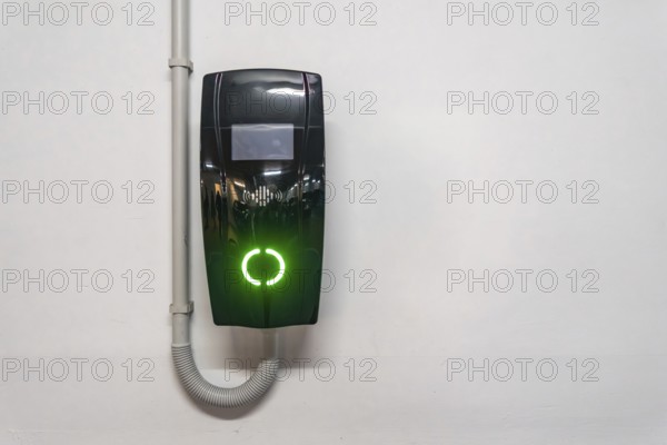 Electric vehicle wallbox charger mounted on a white wall in valencia, spain, glowing bright green