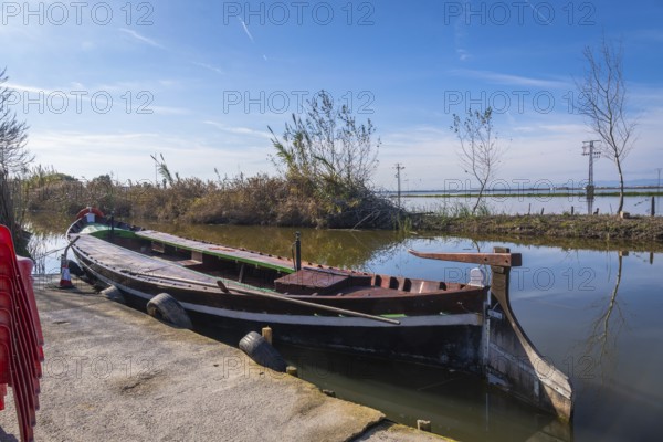 Traditional barca de l'albufera moored at a concrete pier in historic el palmar, reflecting