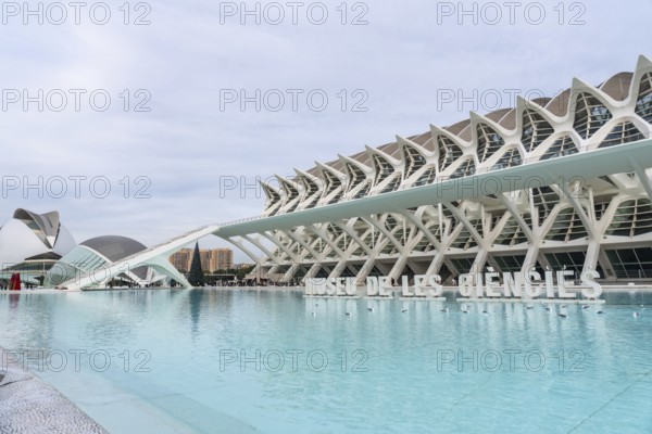 The museu de les ciencies principle building stands prominently against a cloudy sky, reflecting in