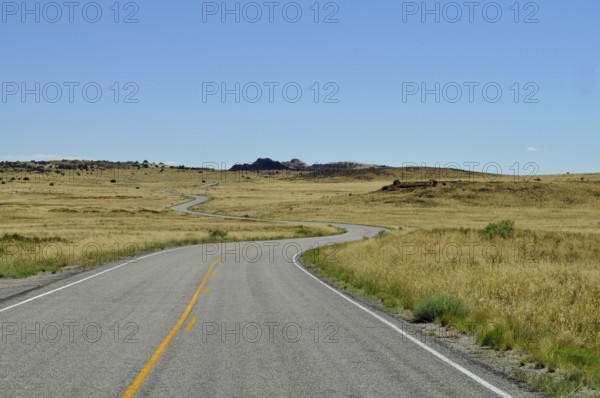 Endless road snakes through a dry desert landscape under a clear blue sky, Canyonlands National