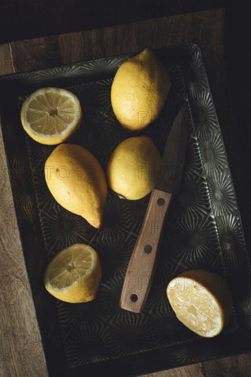 A rustic kitchen scene with fresh lemons on a vintage metal tray, accompanied by a wooden handled