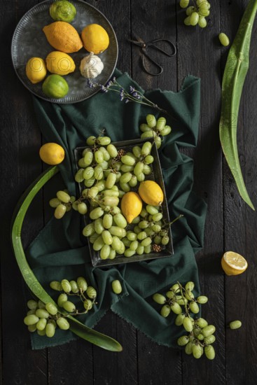 A vibrant display of green grapes, lemons, and limes on a dark wooden surface. The contrasting