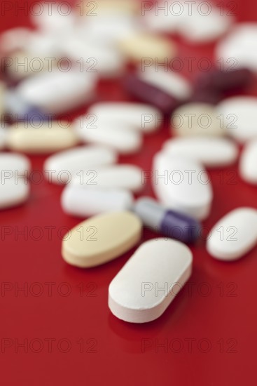 A close-up image of various medical tablets scattered on a bright red background, highlighting