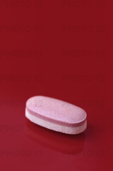 A single pink tablet placed centrally on a vivid red background, conveying a bold contrast that