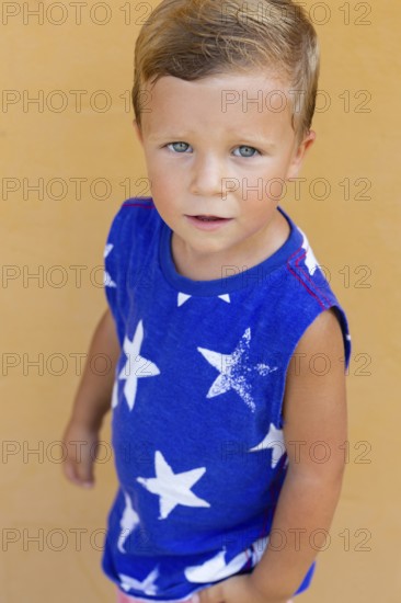 A young boy with blue eyes gazes upwards, wearing a blue shirt with white star patterns His