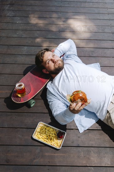 A person enjoying a relaxing moment on a wooden deck, holding a burger. Nearby, there's a