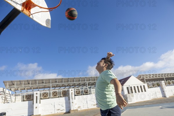 Teenager with Down syndrome playing basketball outdoors, emphasizing sports, captured in an open