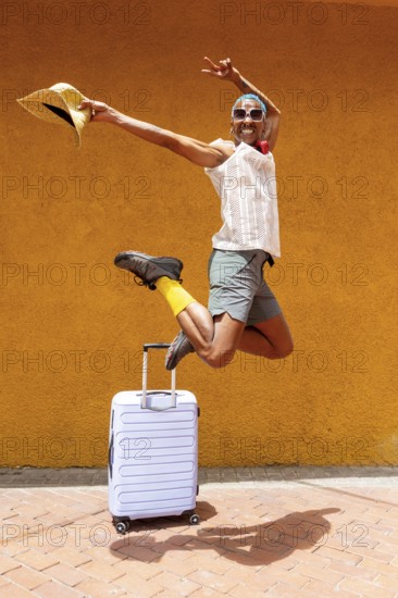 A joyful LGBTQIA+ man jumps exuberantly with a suitcase, ready to embark on a vibrant holiday trip.