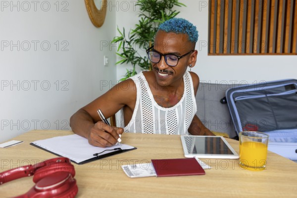 An LGBTQIA+ man enthusiastically prepares for holidays, jotting down plans at a table. Notebooks, a