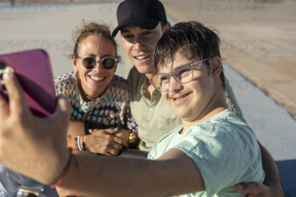 A Down syndrome teenager joyfully taking a selfie with family while enjoying a sunny day outdoors,