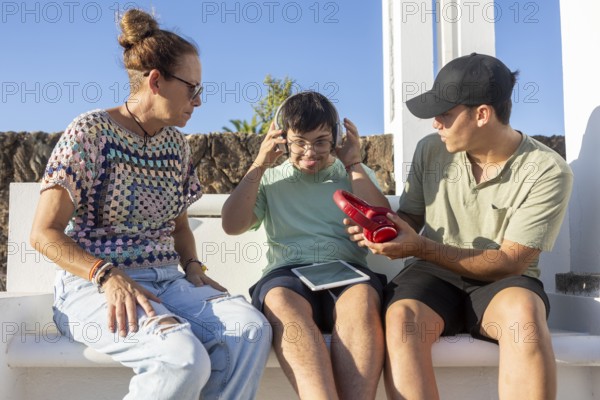 A teenager with Down Syndrome interacting with family outdoors while wearing headphones and holding