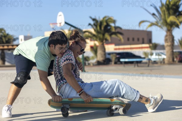 A teenager with Down syndrome helps his mother ride a skateboard outdoors, sharing a fun and