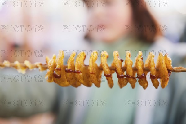 Close-up of golden-brown spiral tornado potatoes on a skewer, drizzled with savory sauce. This