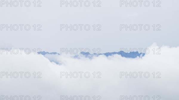 Ethereal view of jagged mountain peaks peering through a blanket of white clouds in San Ramon,