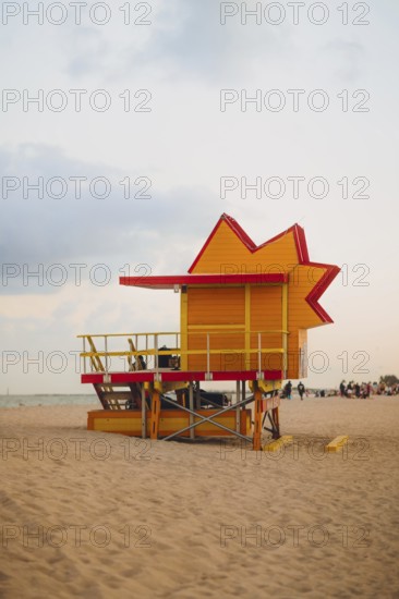 A bright red and yellow lifeguard tower stands vibrantly against a soft dusk sky on Miami Beach,