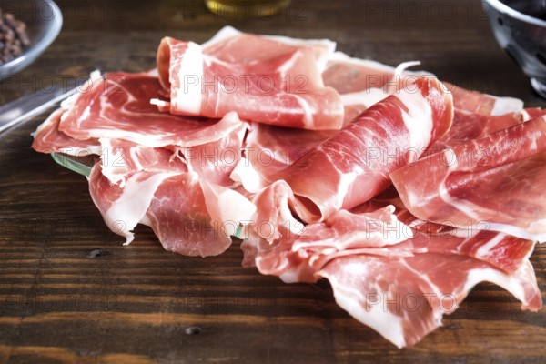 Thin, delicately rolled slices of fresh ham displayed on a dark wooden surface, highlighted by