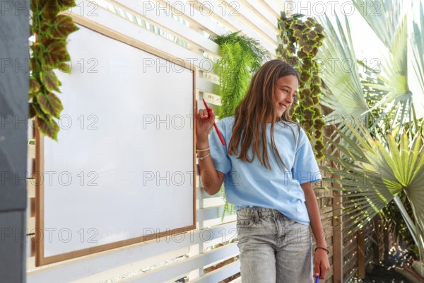 A cheerful young girl stands next to a whiteboard surrounded by lush tropical foliage, holding a